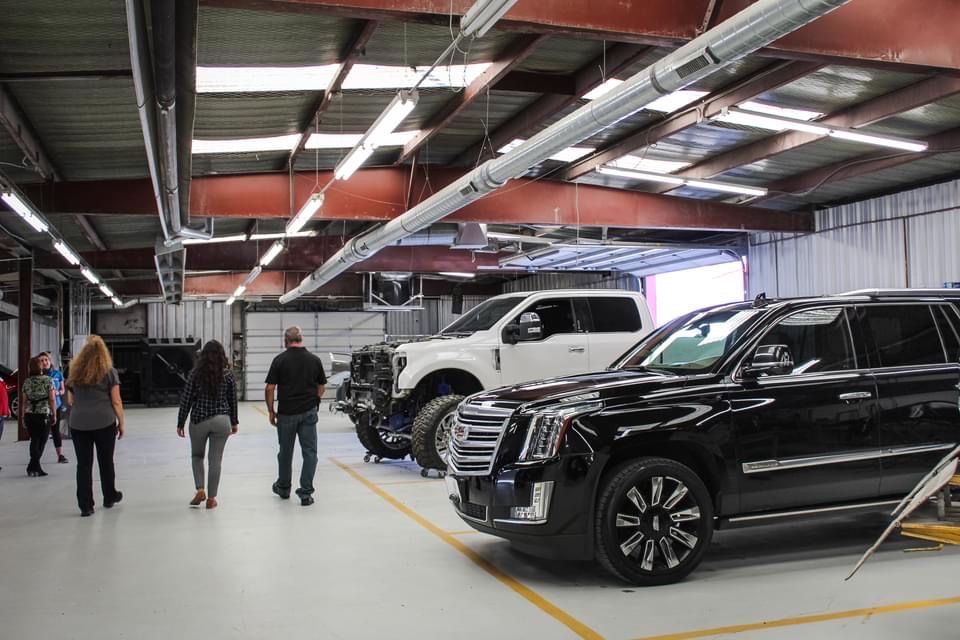 A group of people are standing in a garage looking at cars.