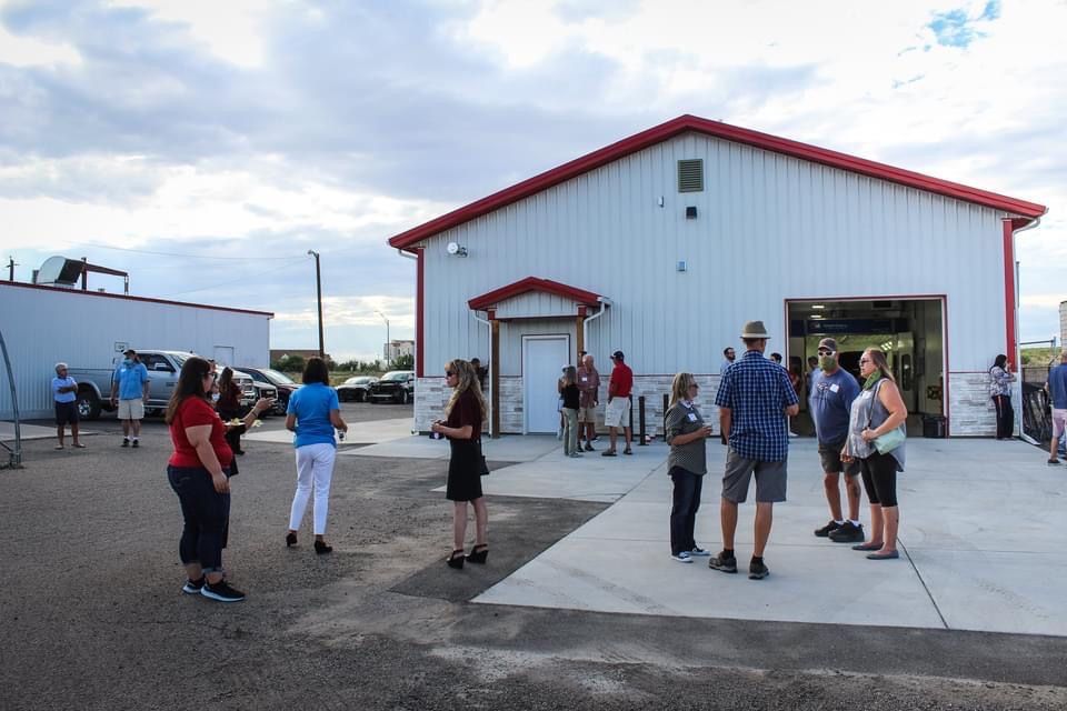 A group of people are standing in front of a large white building with a red roof.