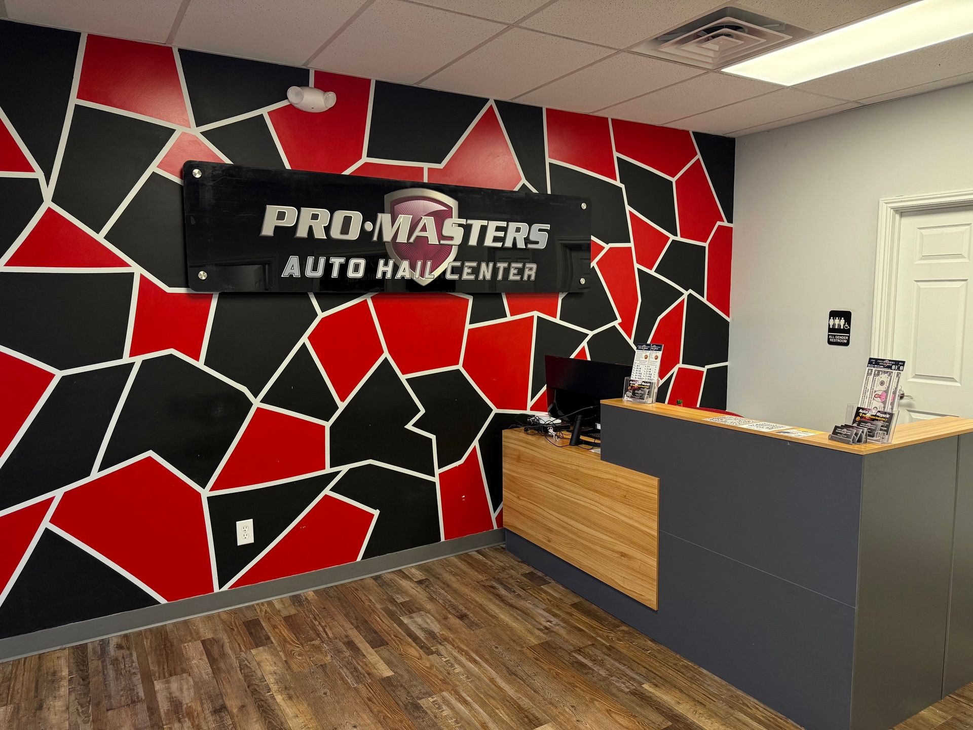Pro-Masters Auto Haul Center reception area with logo on a red and black wall. Wooden counter and floor.