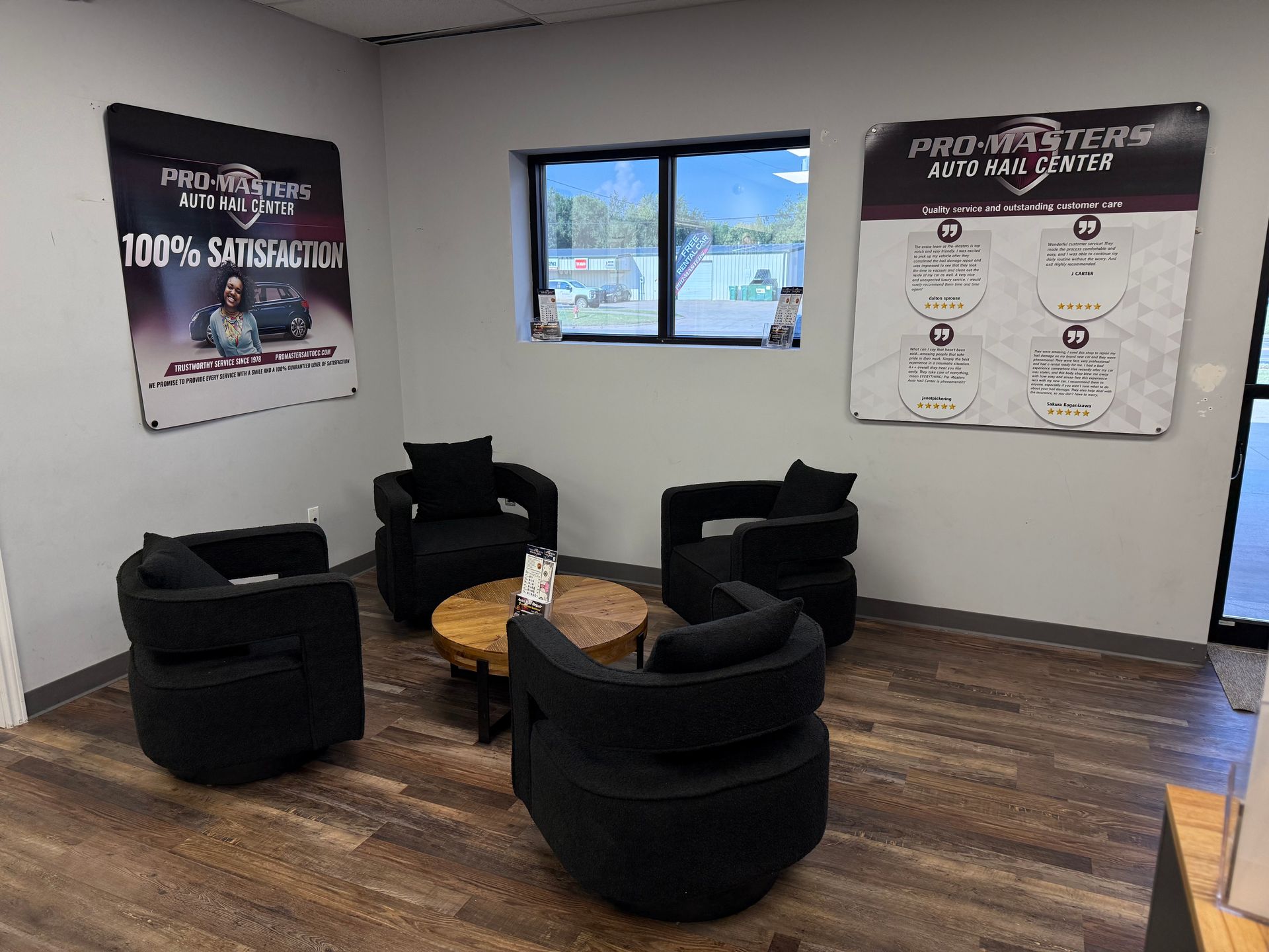 Waiting area with four black armchairs, a round table, and promotional posters.