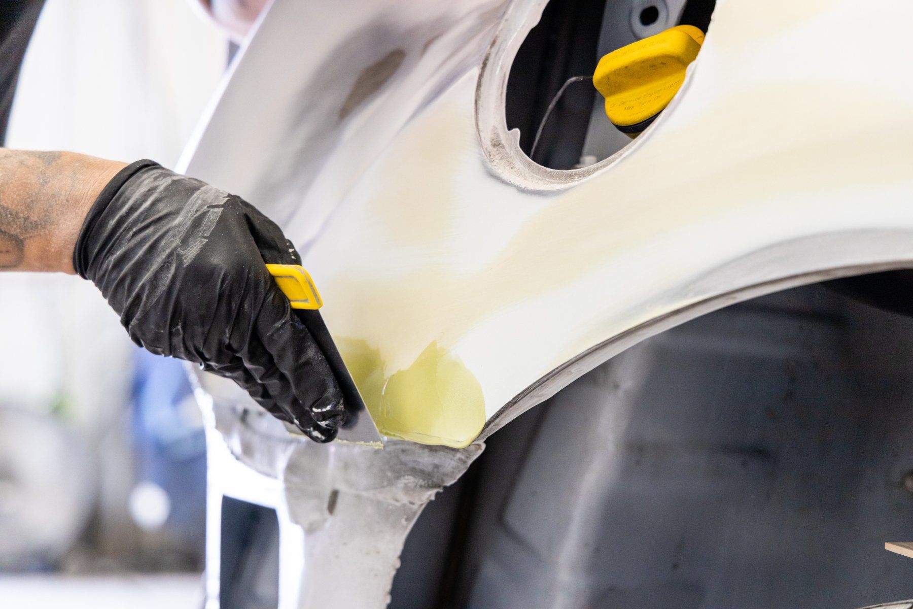 A person is working on a car fender with a spatula.