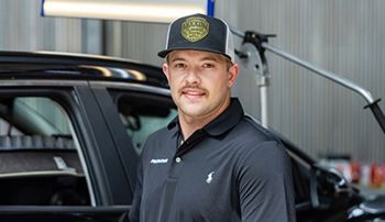 A man wearing a hat is standing in front of a car.