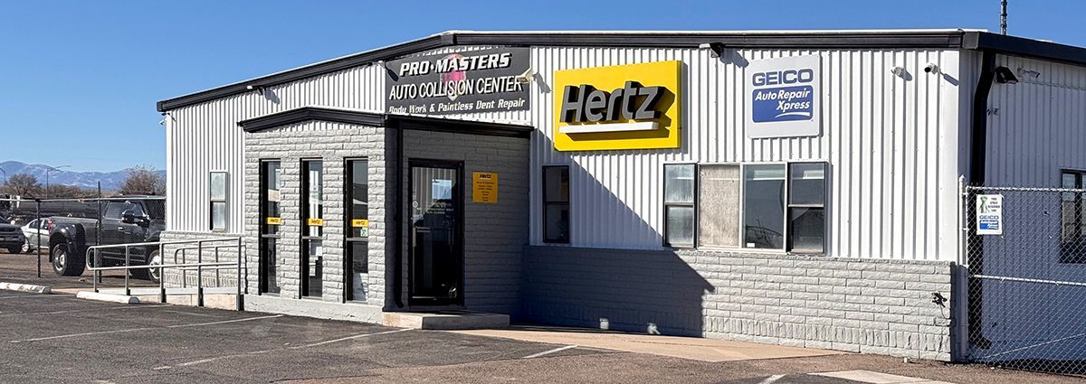 A white building with a yellow sign that says hertz on it.