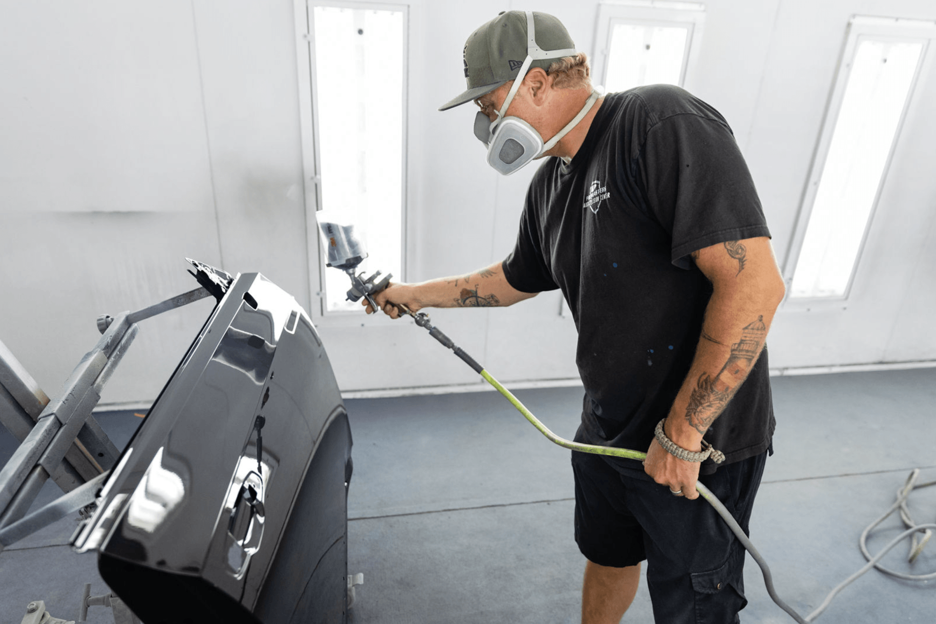 A man wearing a mask is spray painting a car door.