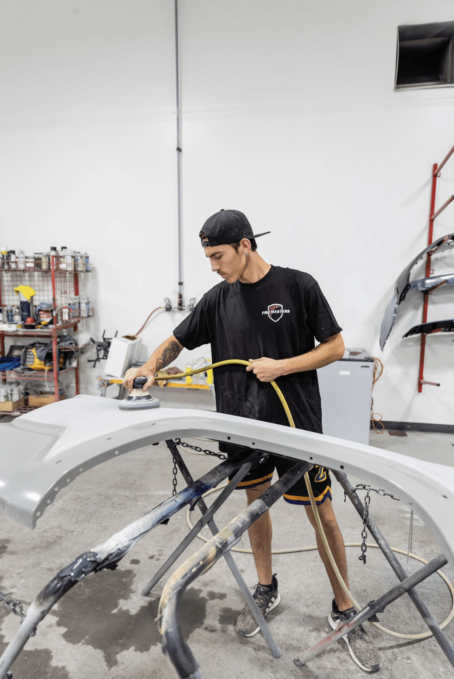 A man is sanding a car bumper in a garage.