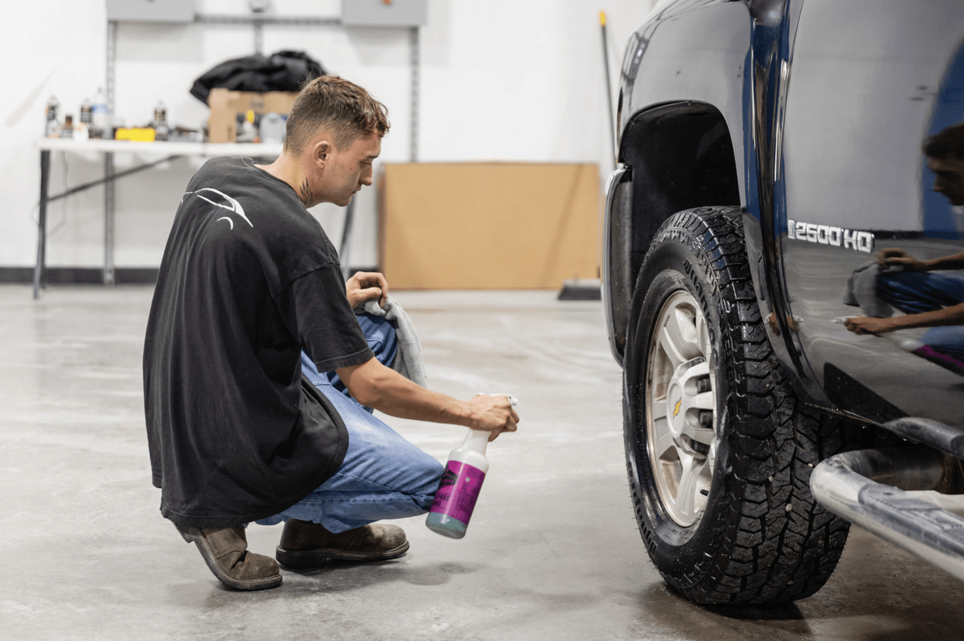 A man is kneeling down next to a truck in a garage.