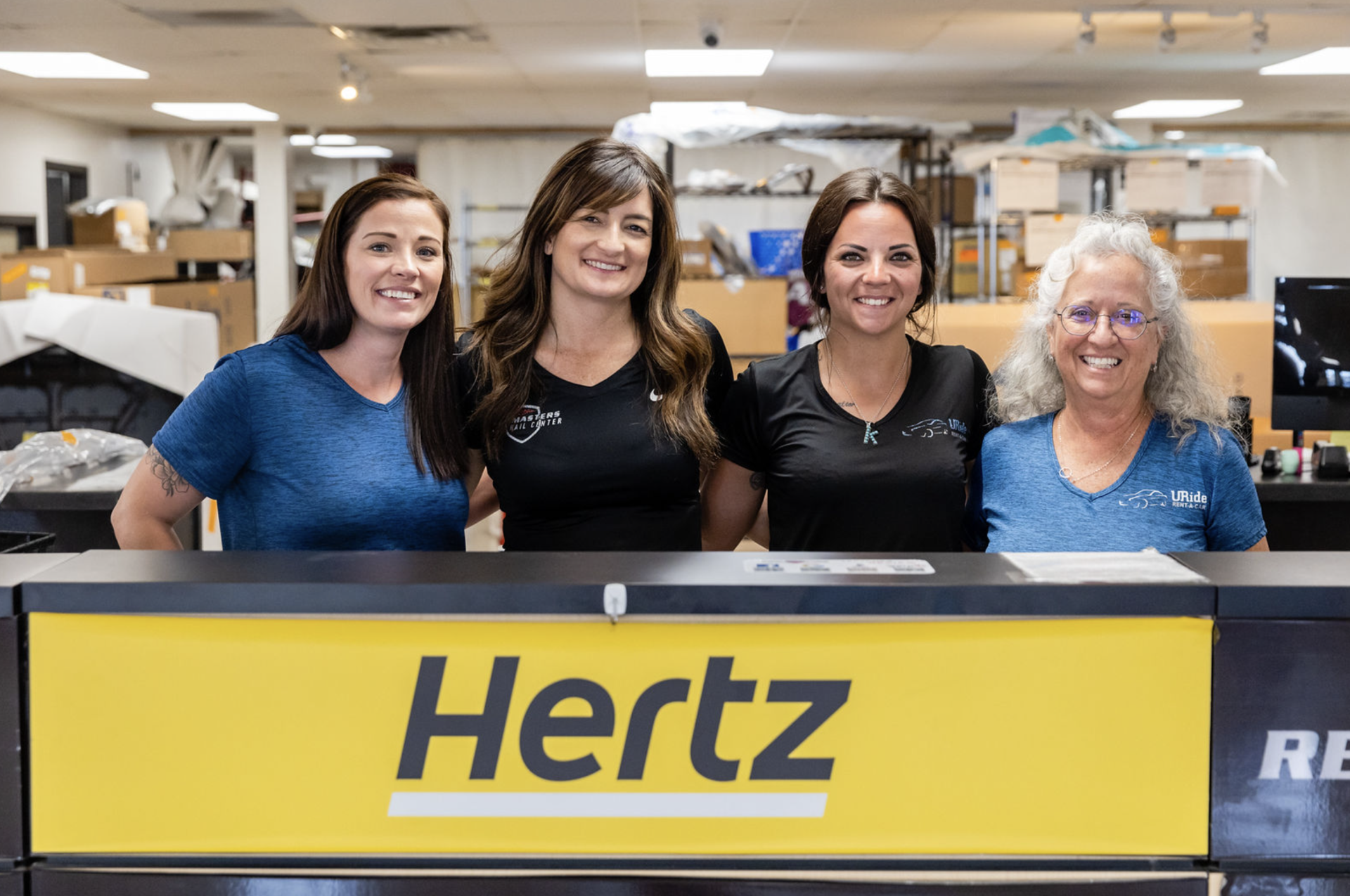 A group of women are posing for a picture in front of a hertz sign.
