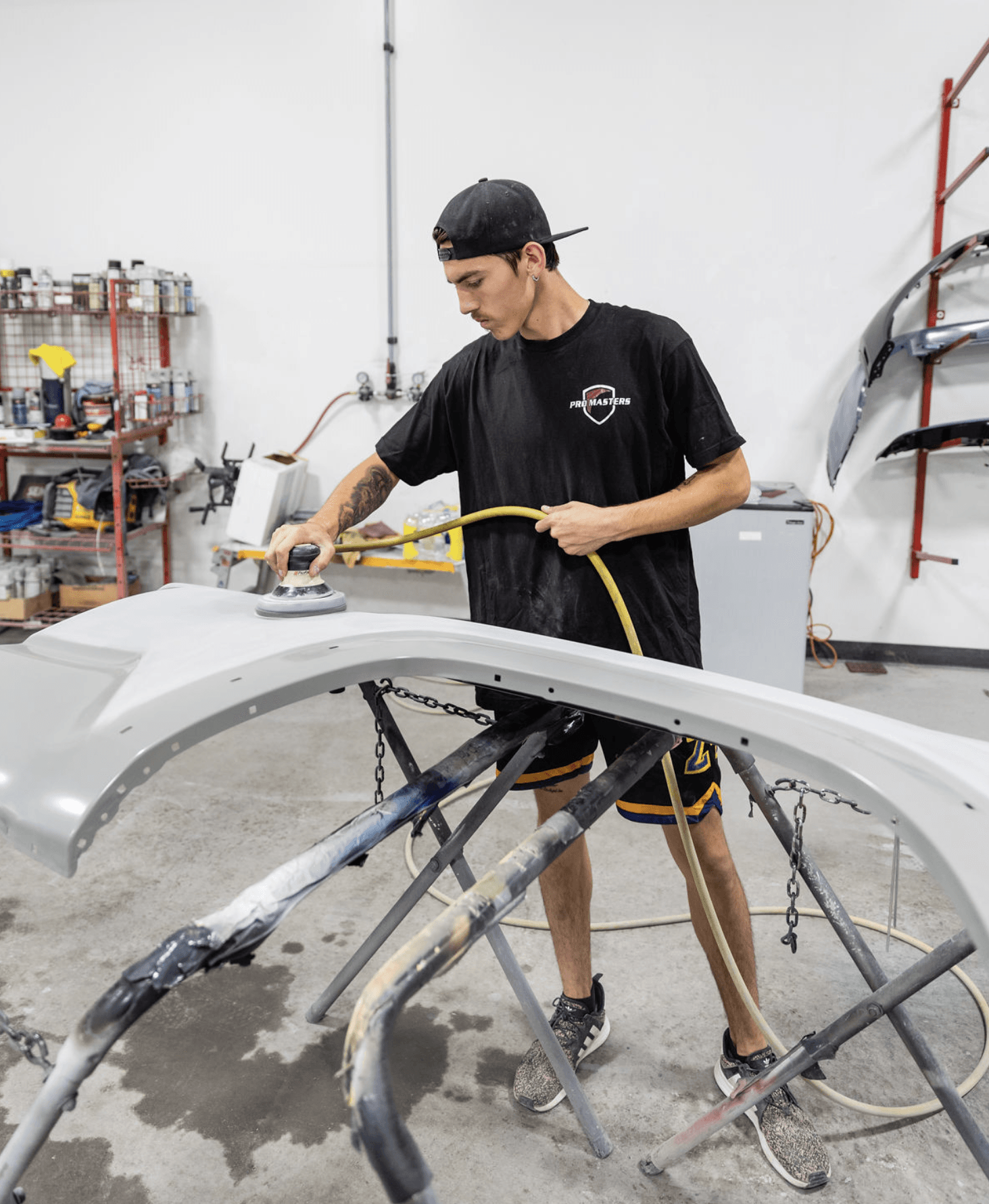 A man is sanding a car bumper in a garage.