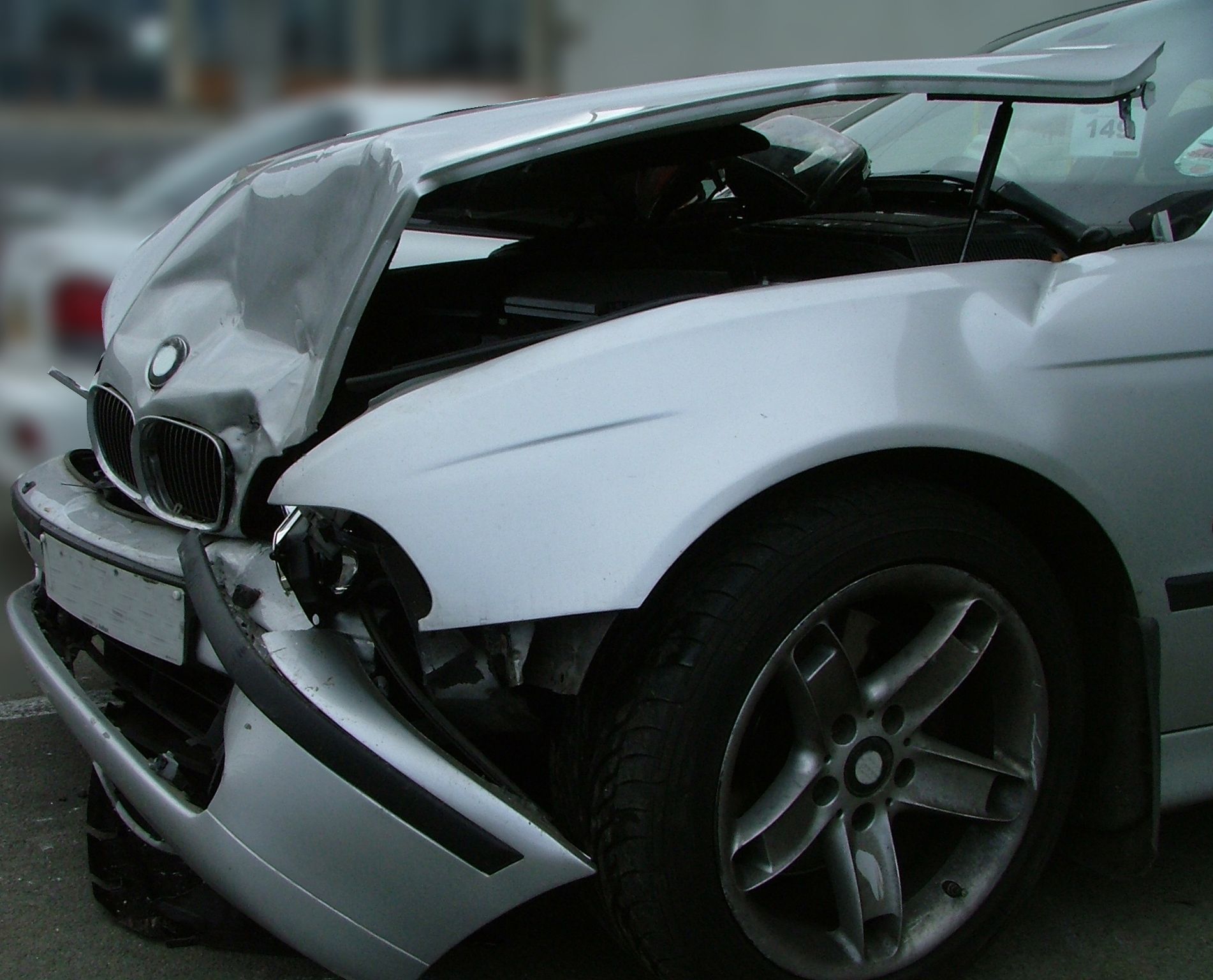 A silver car with the hood open has a damaged bumper