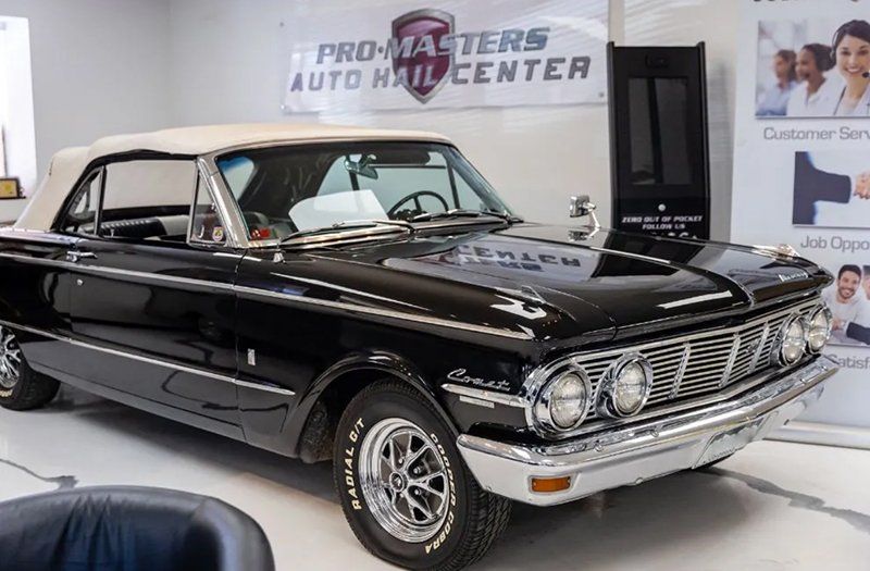 A black car is parked in front of a promasters auto repair center sign.