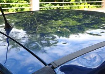 Blue car roof with multiple dents, likely from hail. Antenna and black trim are visible.