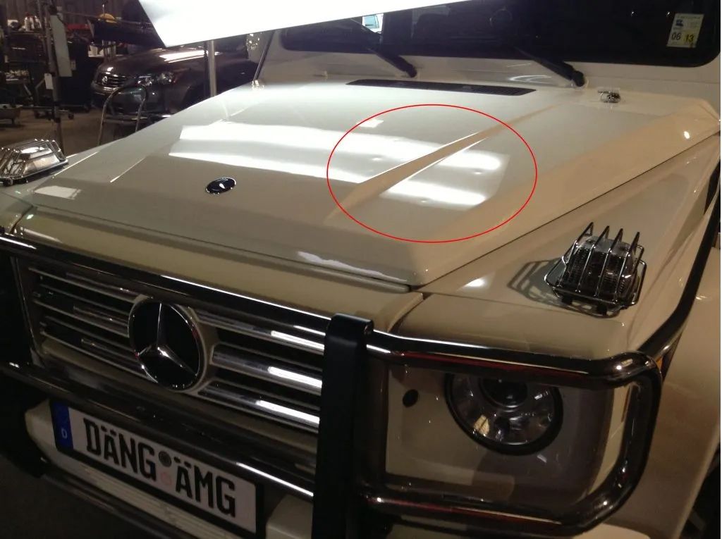 White Mercedes-Benz G-Class hood with a dent, red circle highlights damage.