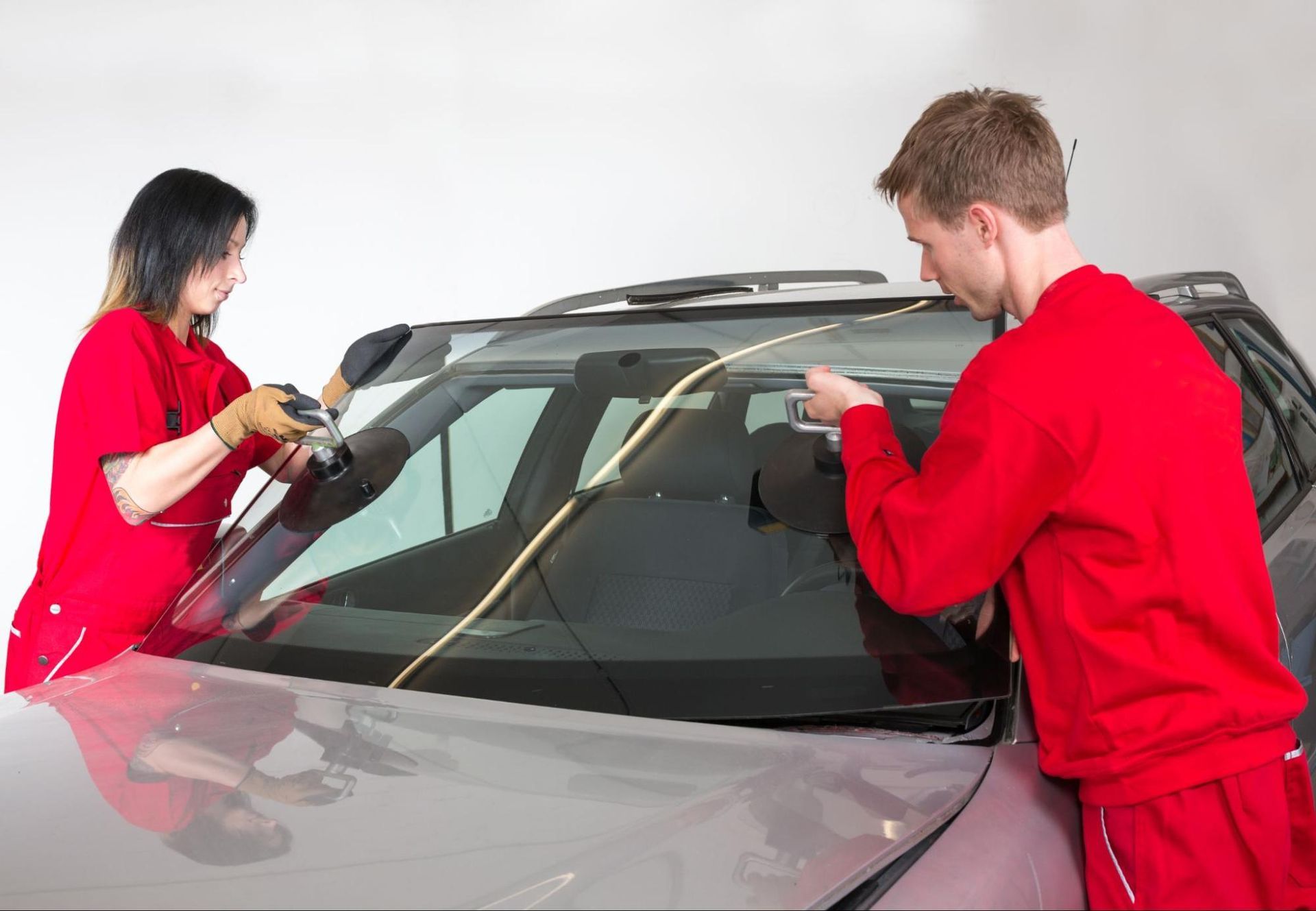 A man and a woman are working on a car windshield