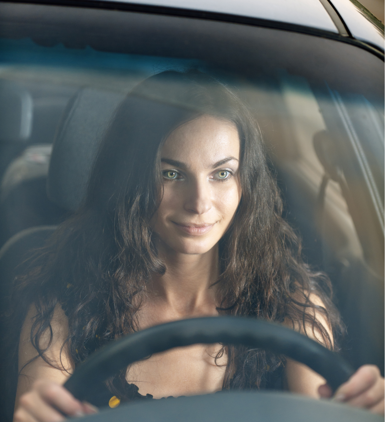A woman is driving a car and smiling at the camera