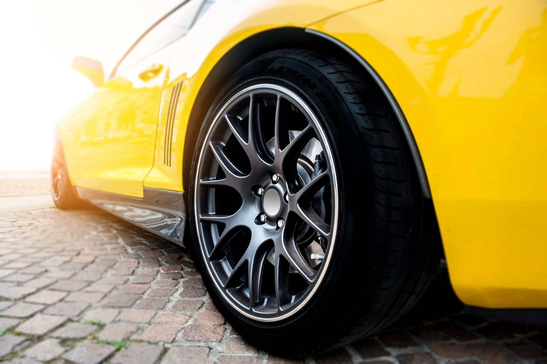 A yellow sports car is parked on a brick sidewalk.