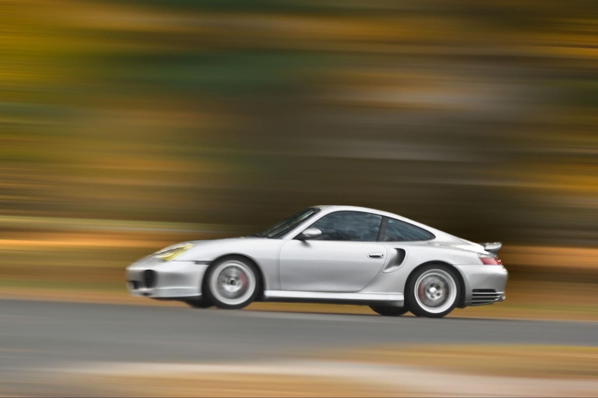 A silver sports car is driving down a road.