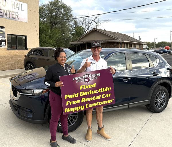 Woman and man holding sign by a blue SUV. The sign reads