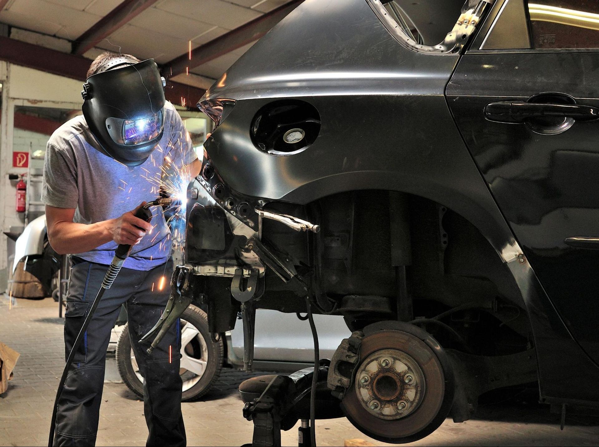 A man wearing a welding helmet is welding a car in a garage.