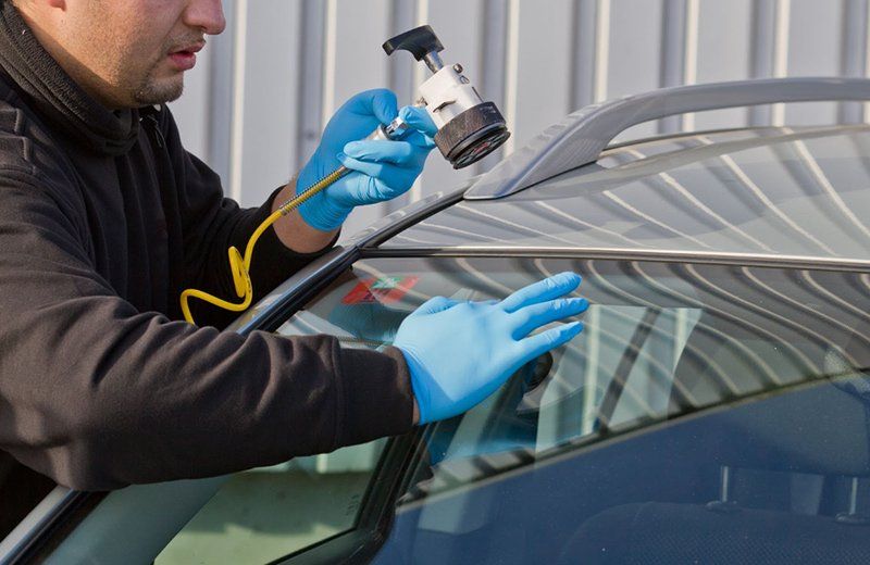 A man wearing blue gloves is fixing a windshield on a car.