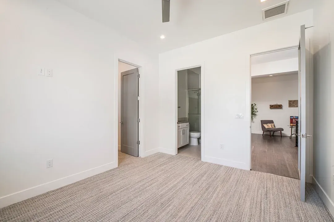 An empty bedroom with a carpeted floor and a ceiling fan.