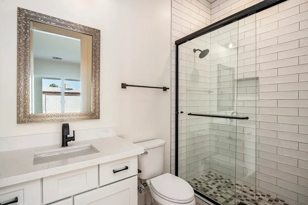 A bathroom with a toilet , sink , mirror and walk in shower.