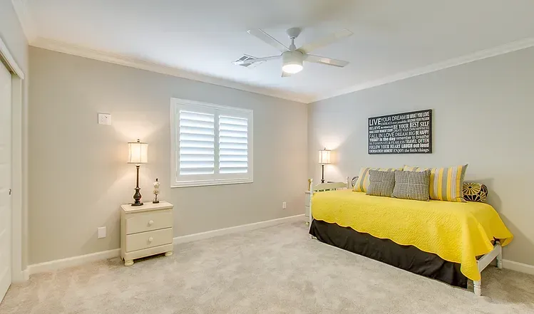 A bedroom with a yellow bed and a ceiling fan.