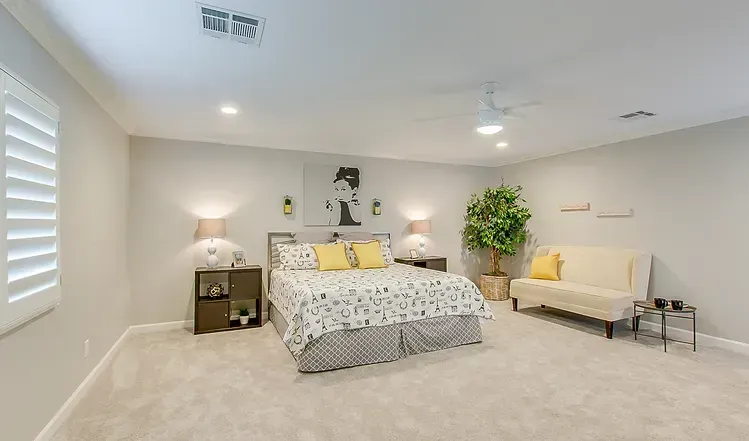 A bedroom with a king size bed , couch , nightstands , and a ceiling fan.