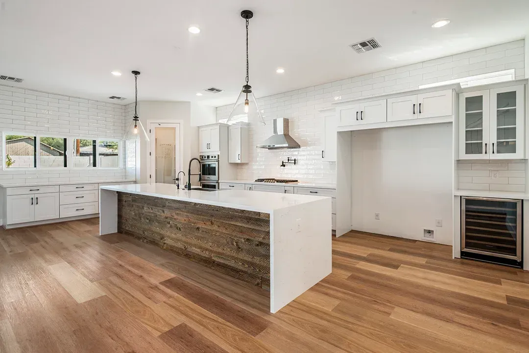 A kitchen with hardwood floors , white cabinets , and a large island.