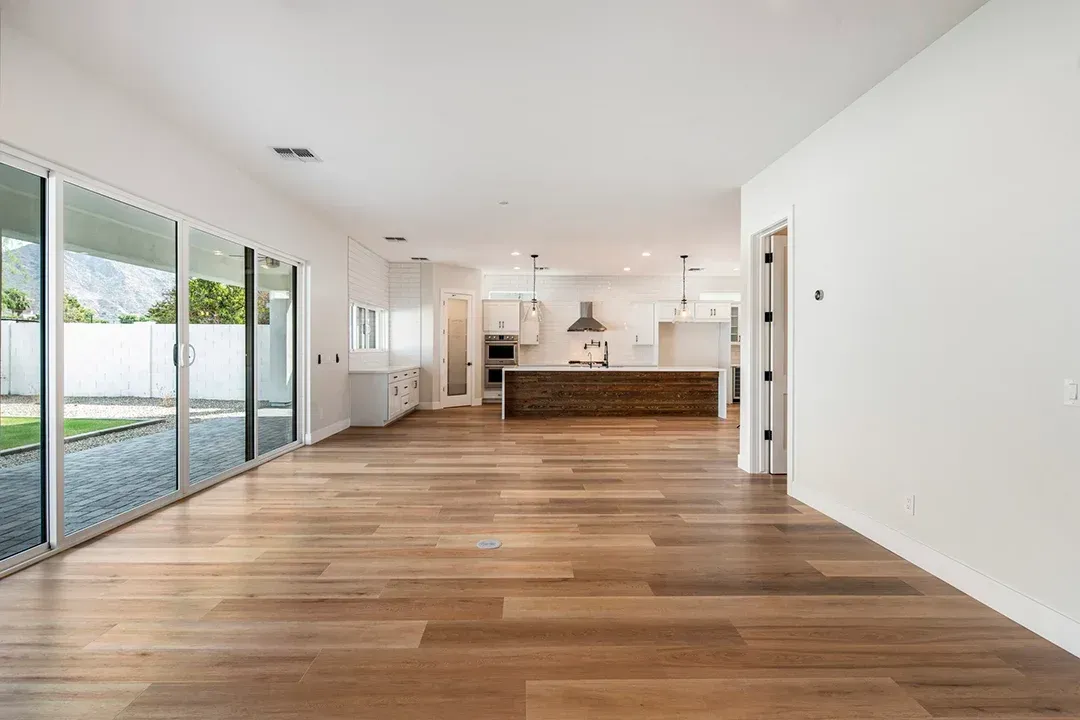 An empty living room with hardwood floors and sliding glass doors leading to a kitchen.