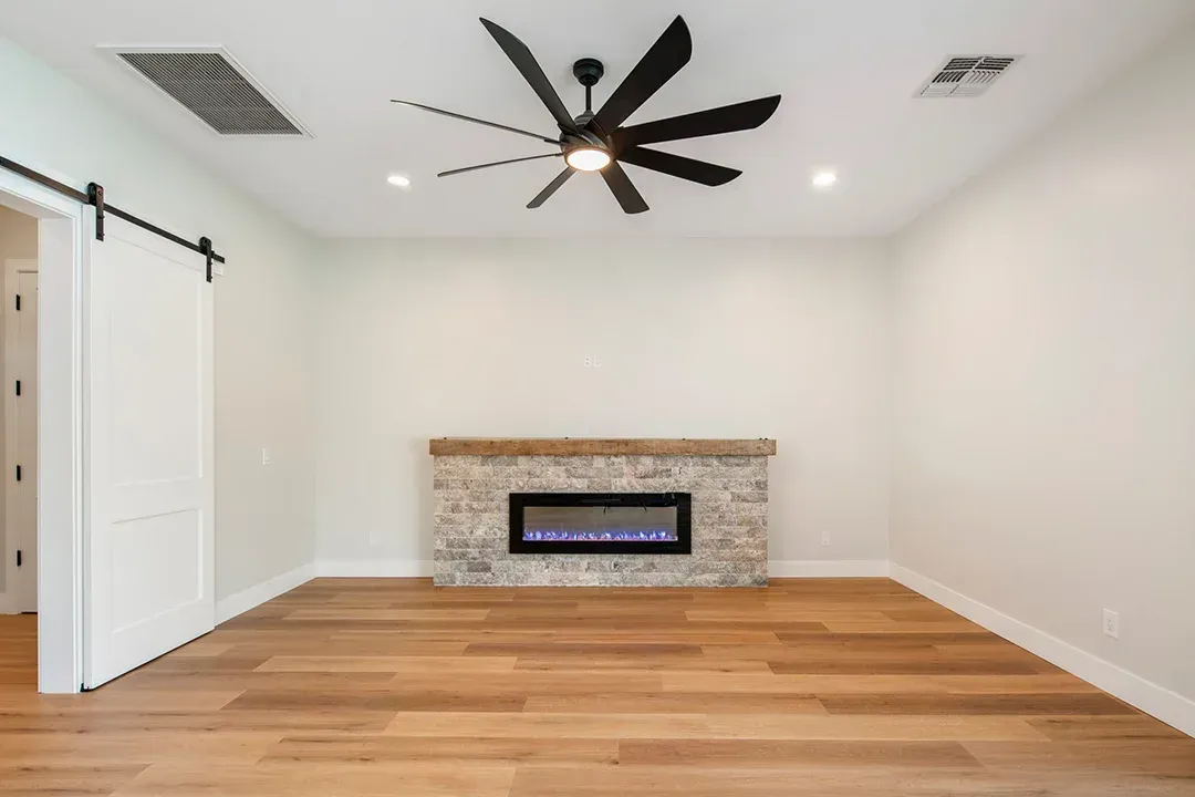 An empty living room with a fireplace and ceiling fan.