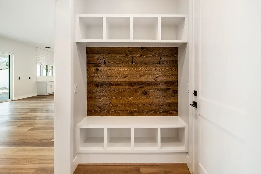 A mud room with a wooden wall and white shelves.