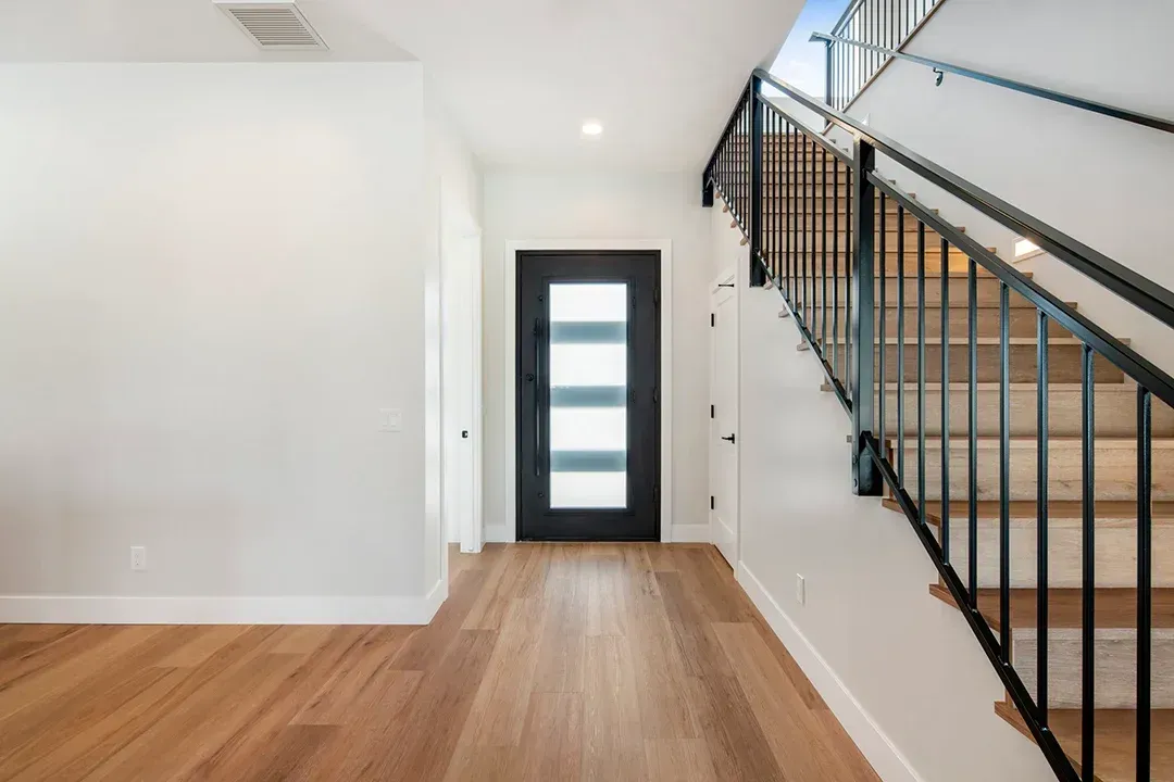 A hallway with a black door and stairs in a house