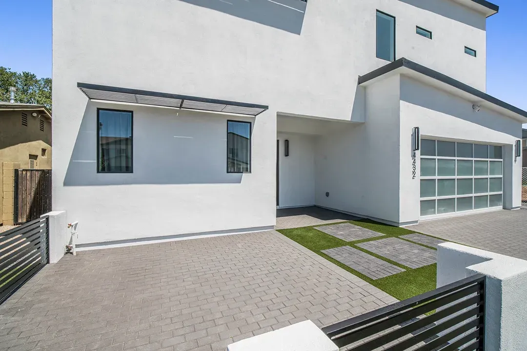 A white house with a large garage and a fence in front of it.