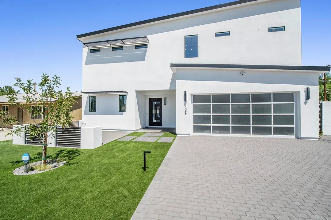 A white house with a glass garage door and a brick driveway.