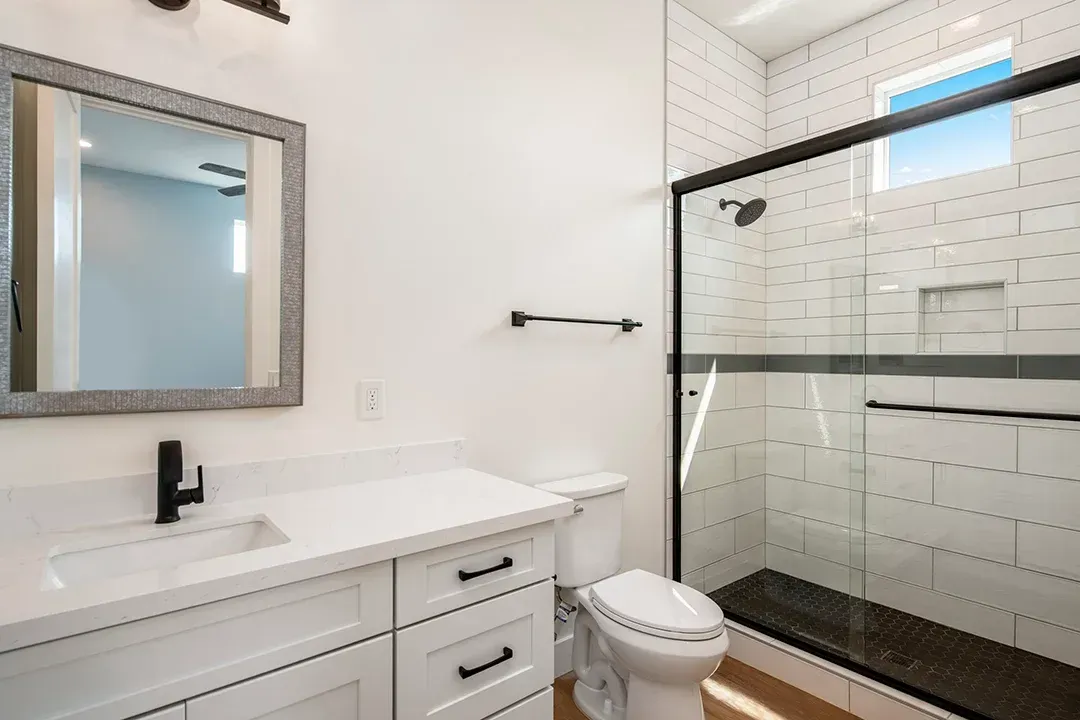 A bathroom with a toilet , sink , mirror and shower.