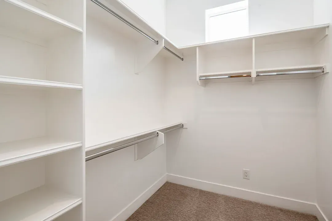 An empty walk in closet with white shelves and a window.