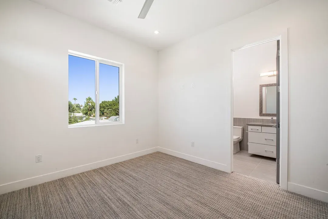 An empty bedroom with a bathroom and a window.