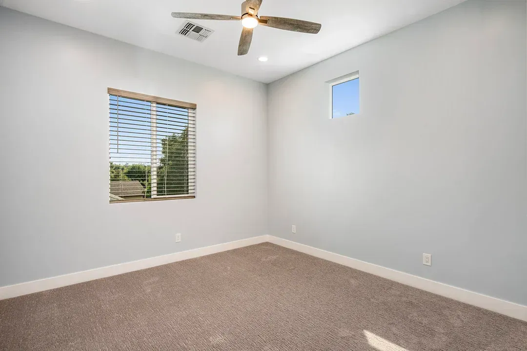 An empty bedroom with a ceiling fan and a window.