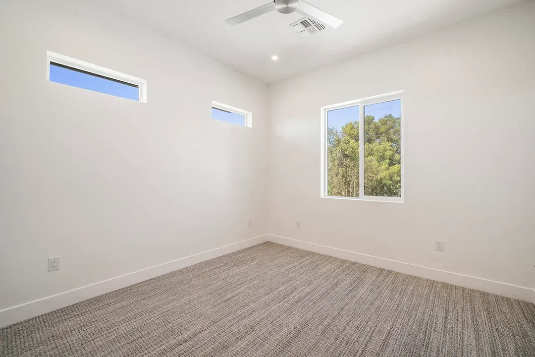 An empty bedroom with two windows and a ceiling fan.