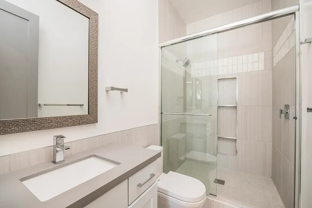 A bathroom with a toilet , sink , mirror and walk in shower.