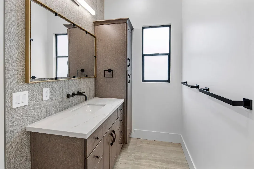 A bathroom with a sink , mirror and window.