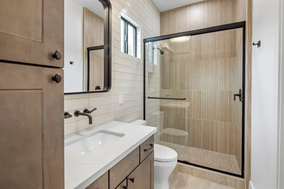 A bathroom with a toilet , sink , mirror and walk in shower.