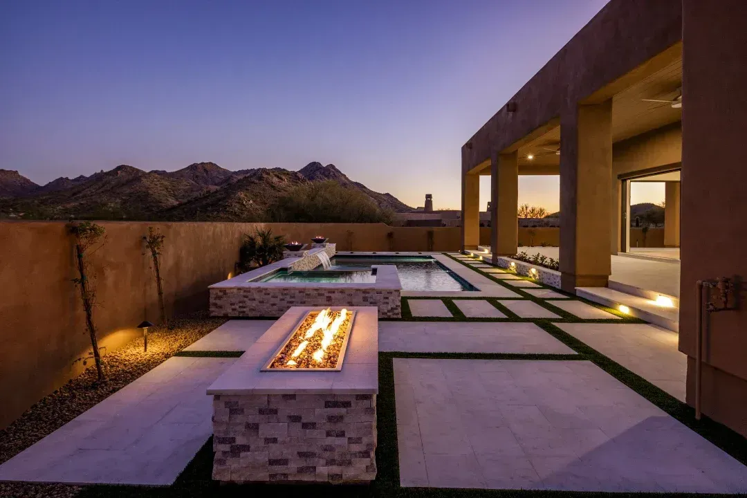 A fire pit is in the middle of a patio next to a pool.