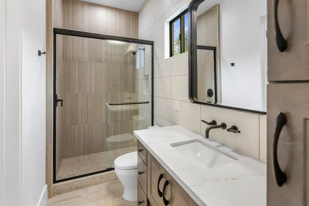 A bathroom with a toilet , sink , mirror and walk in shower.