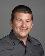 A man in a gray shirt is smiling for the camera.