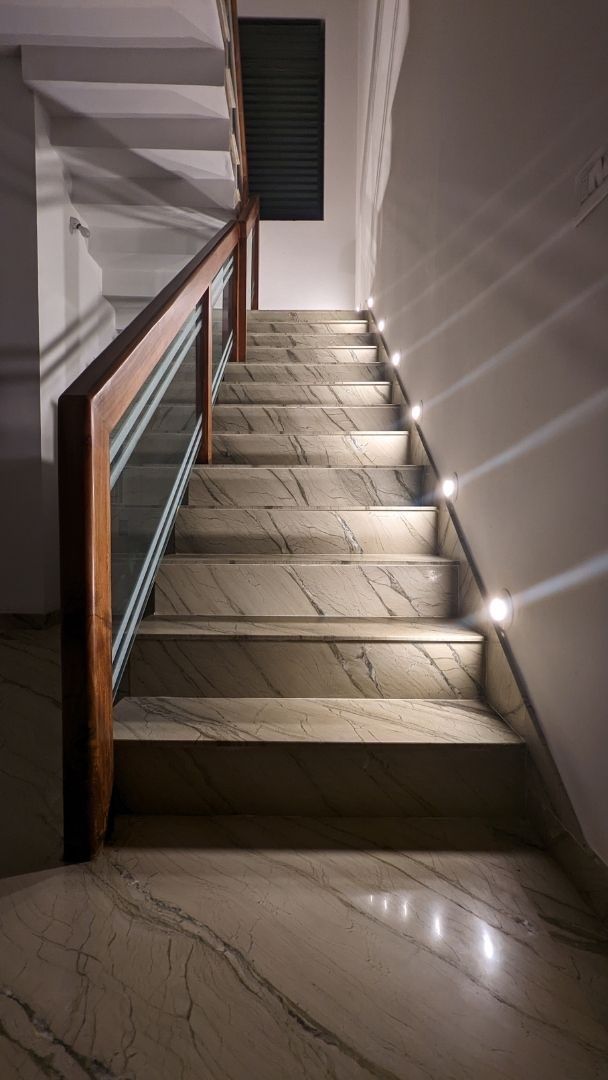 A staircase with marble steps and a wooden railing is lit up at night.