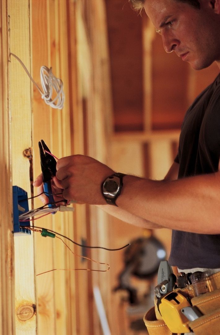 A man is working on electrical wires on a wall.