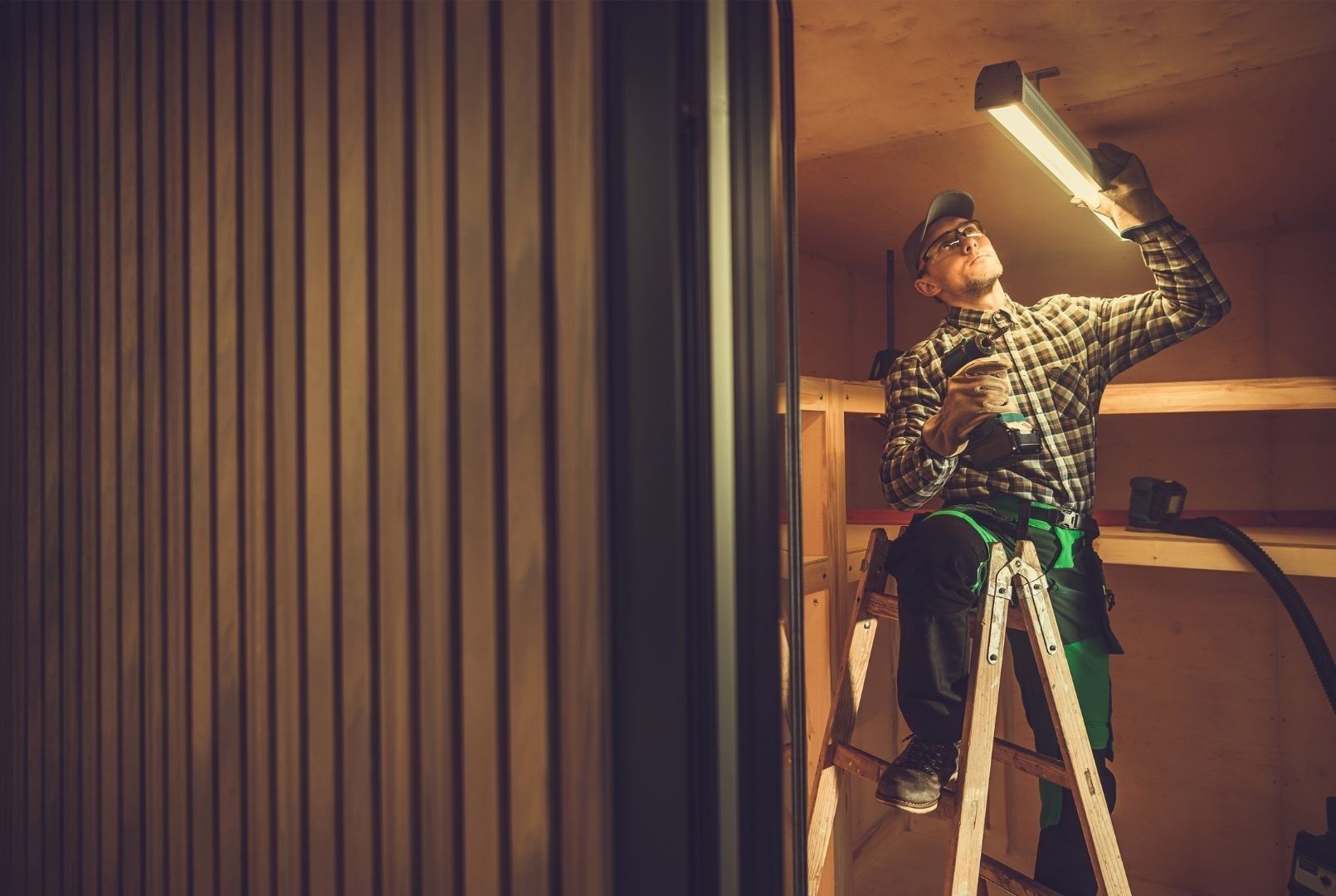 A man is standing on a ladder looking at a light.