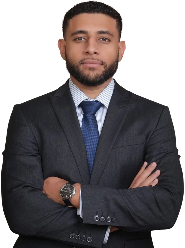 Man in a dark suit with blue tie, standing with arms crossed against a white background