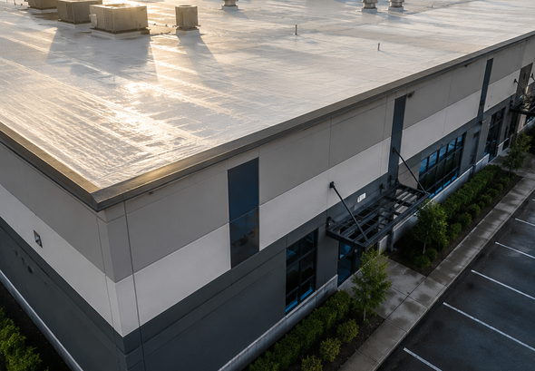 Aerial view of a white industrial building with a reflective roof and adjacent parking lot